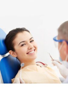 a woman sitting on a blue dental chair flashing a beautiful smile while the back of head of his dentist is visible